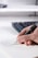 A hand is holding a pen and writing on a notebook page. The paper has a diagram and some handwritten text. A keyboard is visible in the background, slightly out of focus.