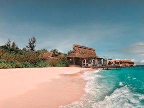 A serene Maldivian beach with turquoise water and a small local guesthouse in the background.