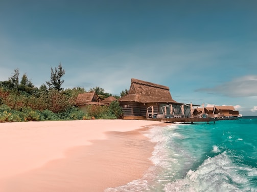 A serene Maldivian beach with turquoise water and a small local guesthouse in the background.