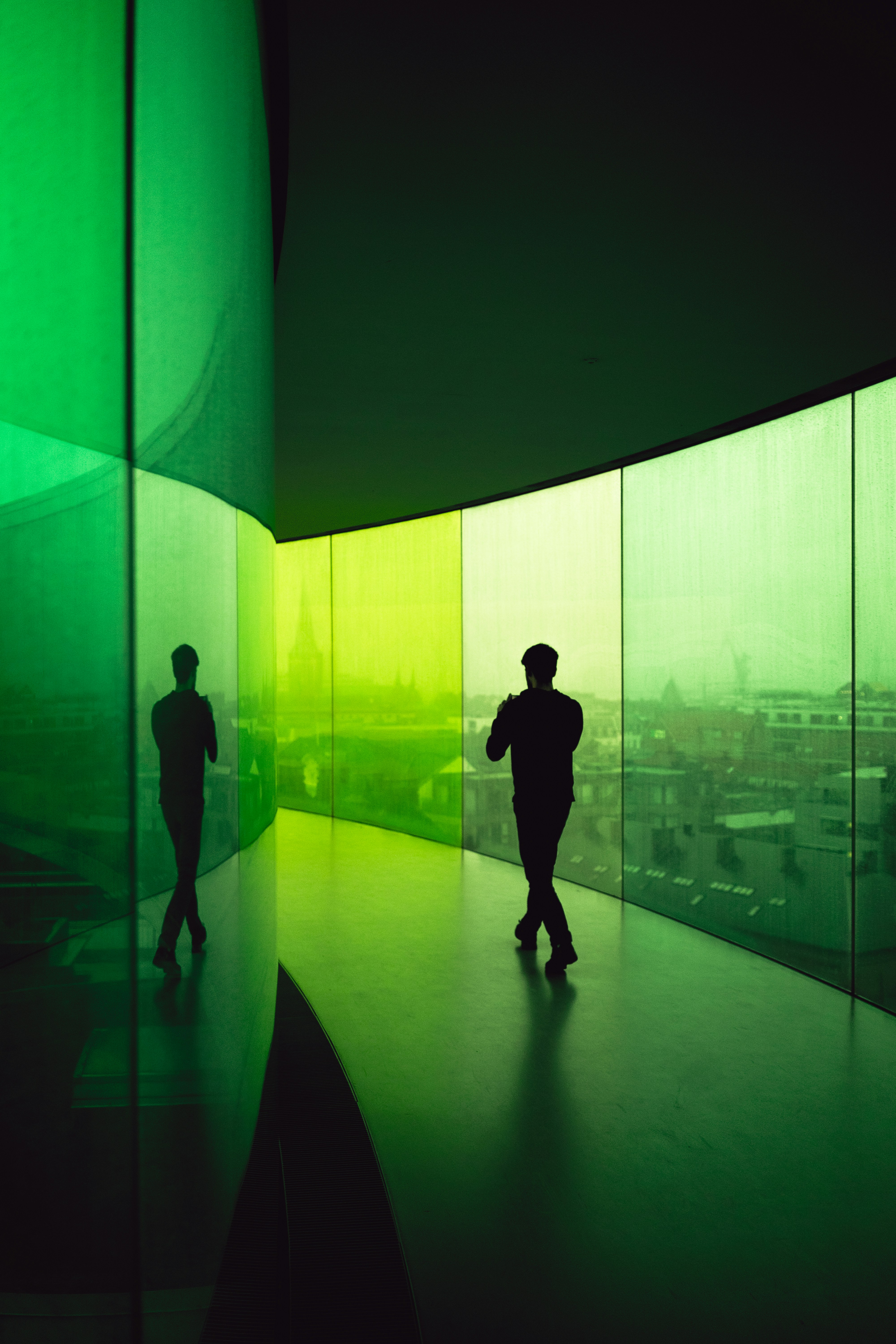 A person walks through a modern glass corridor overlooking the city.