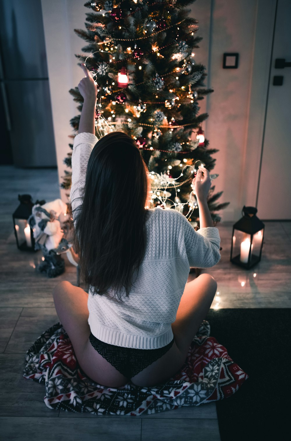 woman sits on red textile infront of Christmas tree