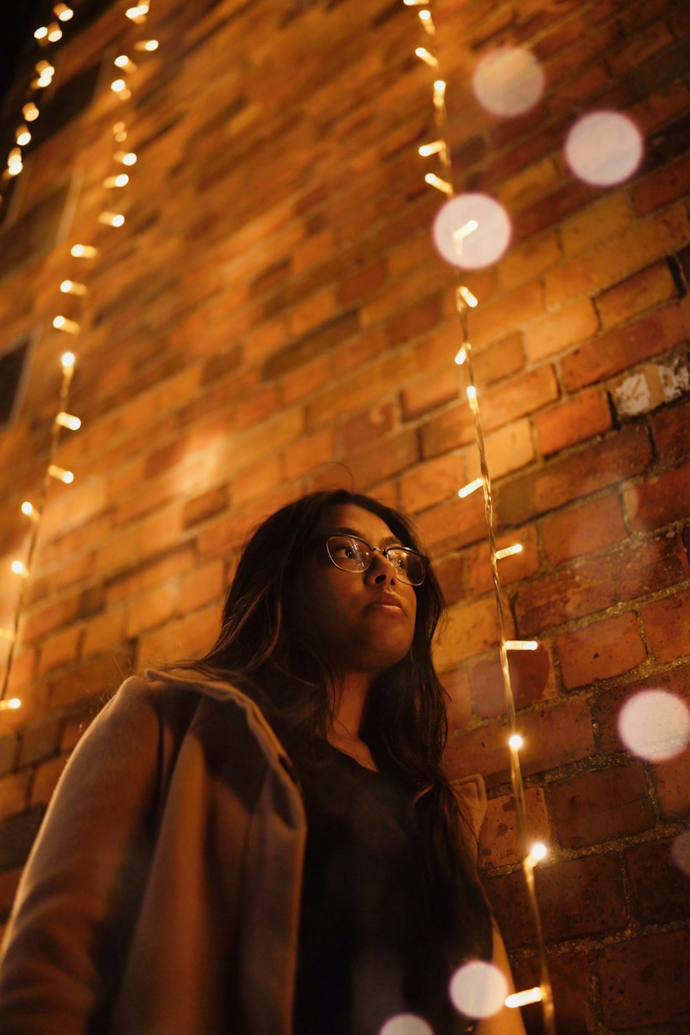 woman wearing eyeglasses beside string lights