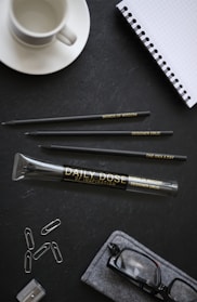 A bright desk setup featuring a sleek pen holder filled with various durable pens beside a neat stack of notebooks.