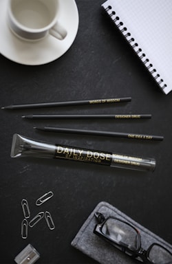 Colorful personalized agendas neatly arranged on a wooden desk with pens and a coffee cup.