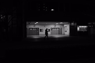 A security guard patrolling a commercial building entrance at dusk.
