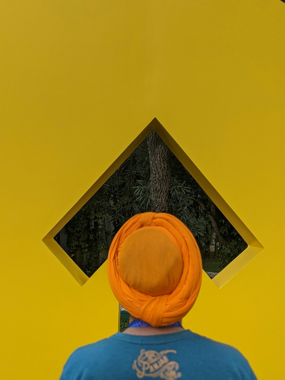 person wearing blue and brown shirt and orange turban hat standing while facing back