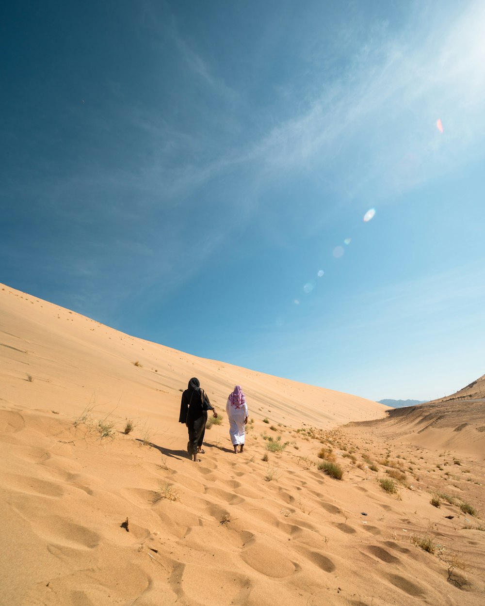 two people walking on desert under blue and white sky