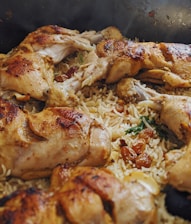 Golden brown roasted chicken drumsticks are placed over a bed of fluffy basmati rice. The rice is garnished with raisins and herbs, adding texture and color to the dish.