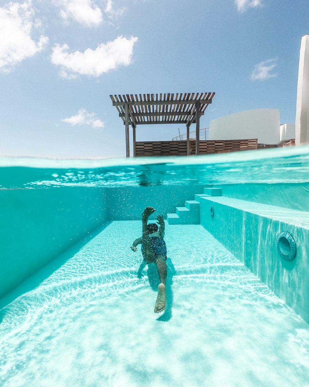 personne nageant dans une piscine verte rectangulaire sous un ciel bleu et blanc