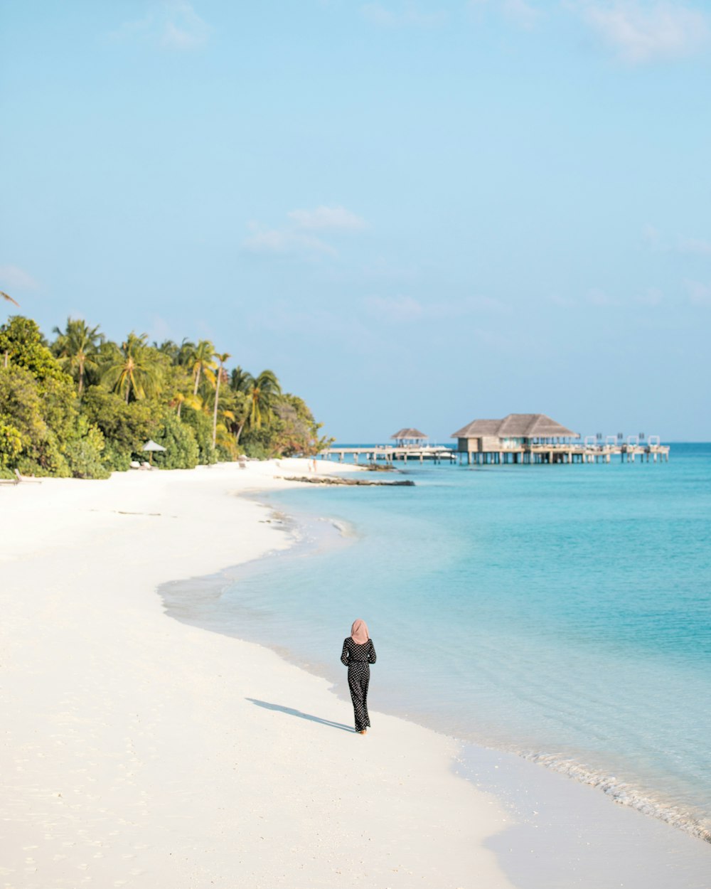 person standing on seashore viewing blue sea under blue and white sky