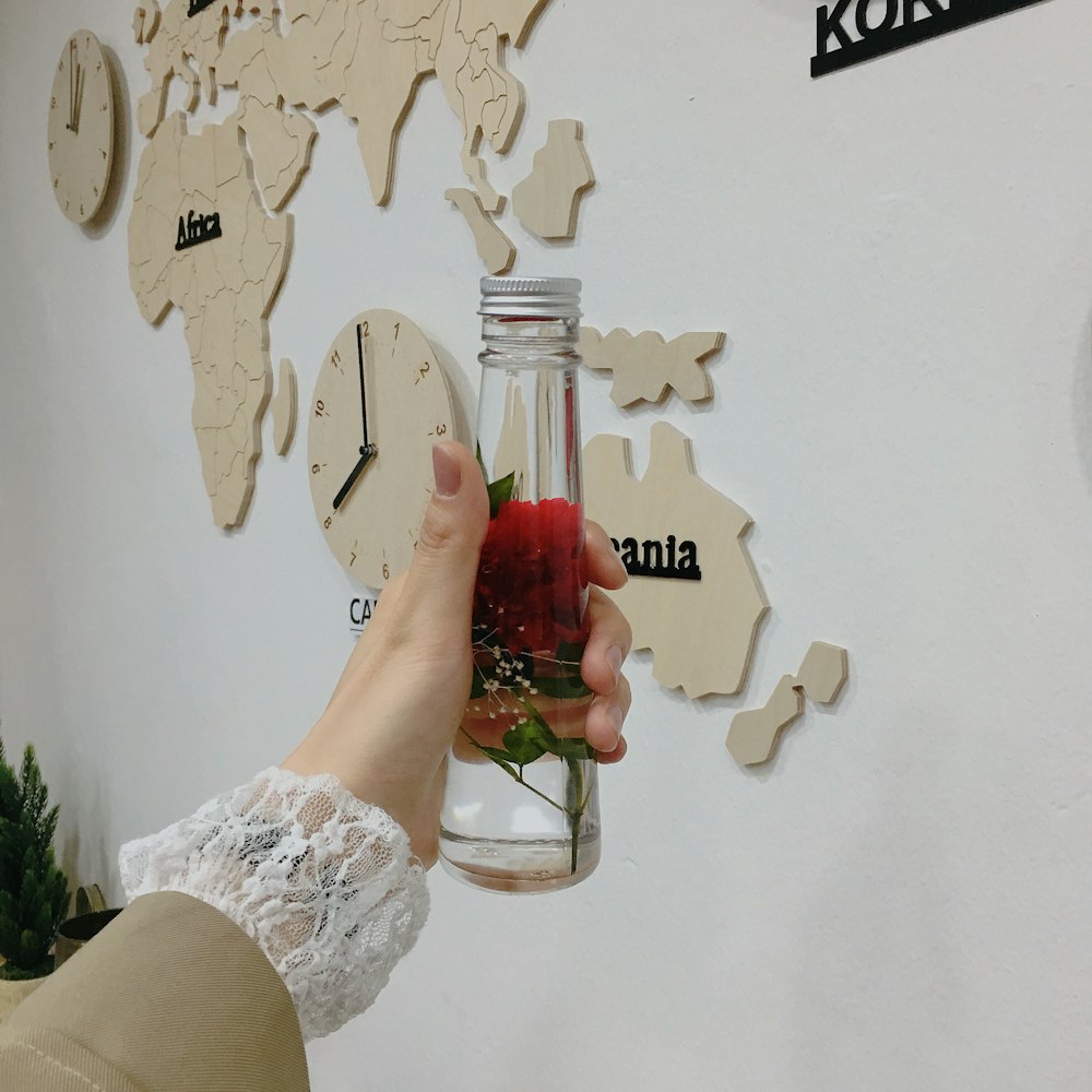 person holding red flower inside closed bottle
