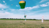 Skydiver landing gracefully on a grassy dropzone with safety orange markers visible.