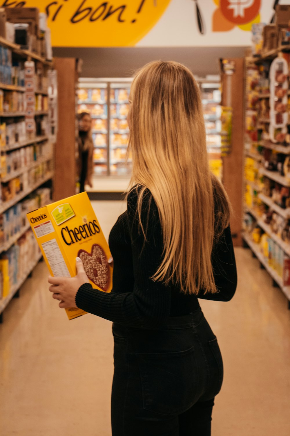 femme portant une chemise noire à manches longues tenant une boîte de céréales Cheerios debout