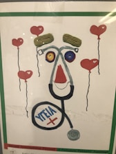 A creative artwork features elements resembling a face made from various objects, including a stethoscope forming the outline, yarn or string for the eyebrows, and colorful circular objects for the eyes. Surrounding the face are floating heart-shaped balloons with red color as the main theme.