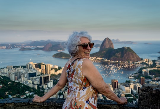 woman wearing yellow, red, and white tank dress leaning on hand rail while smiling in Sugarloaf Mountain Brasil