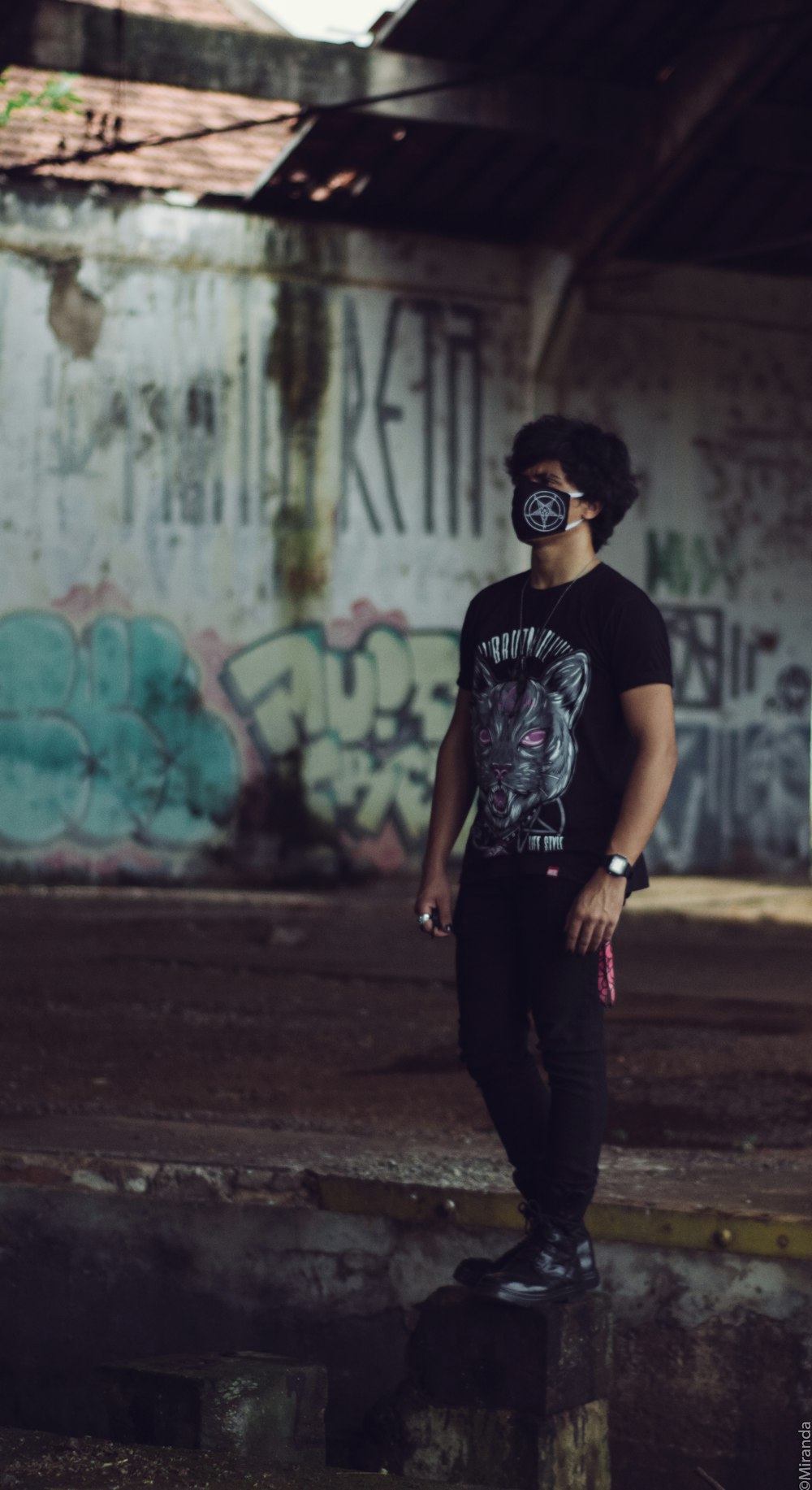 a man wearing a mask standing in front of a graffiti covered wall