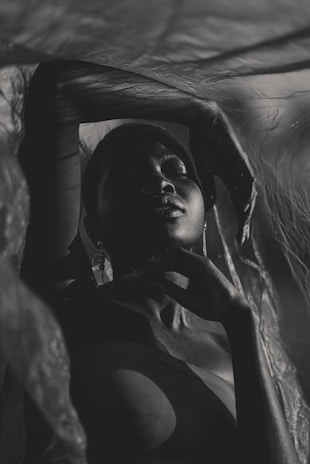 An intimate studio shot featuring a model draped in flowing fabric, with dramatic shadows.