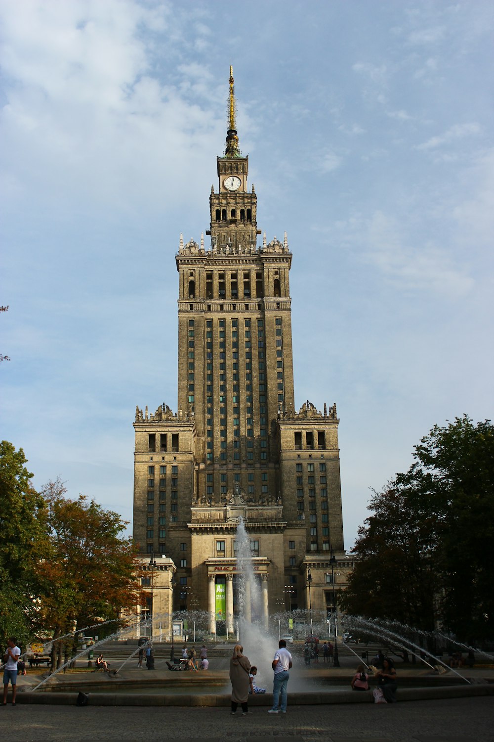 people, water fountain, and building with clock during day