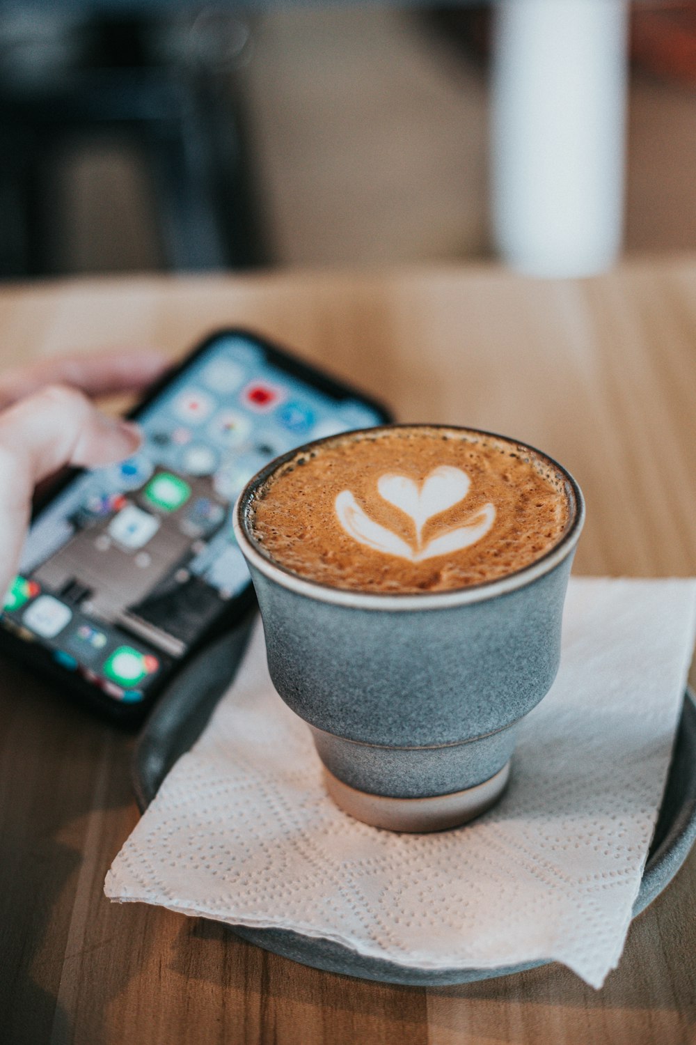 Cappuccino in weißer Tasse auf einer Tischserviette in der Nähe des iPhone 11