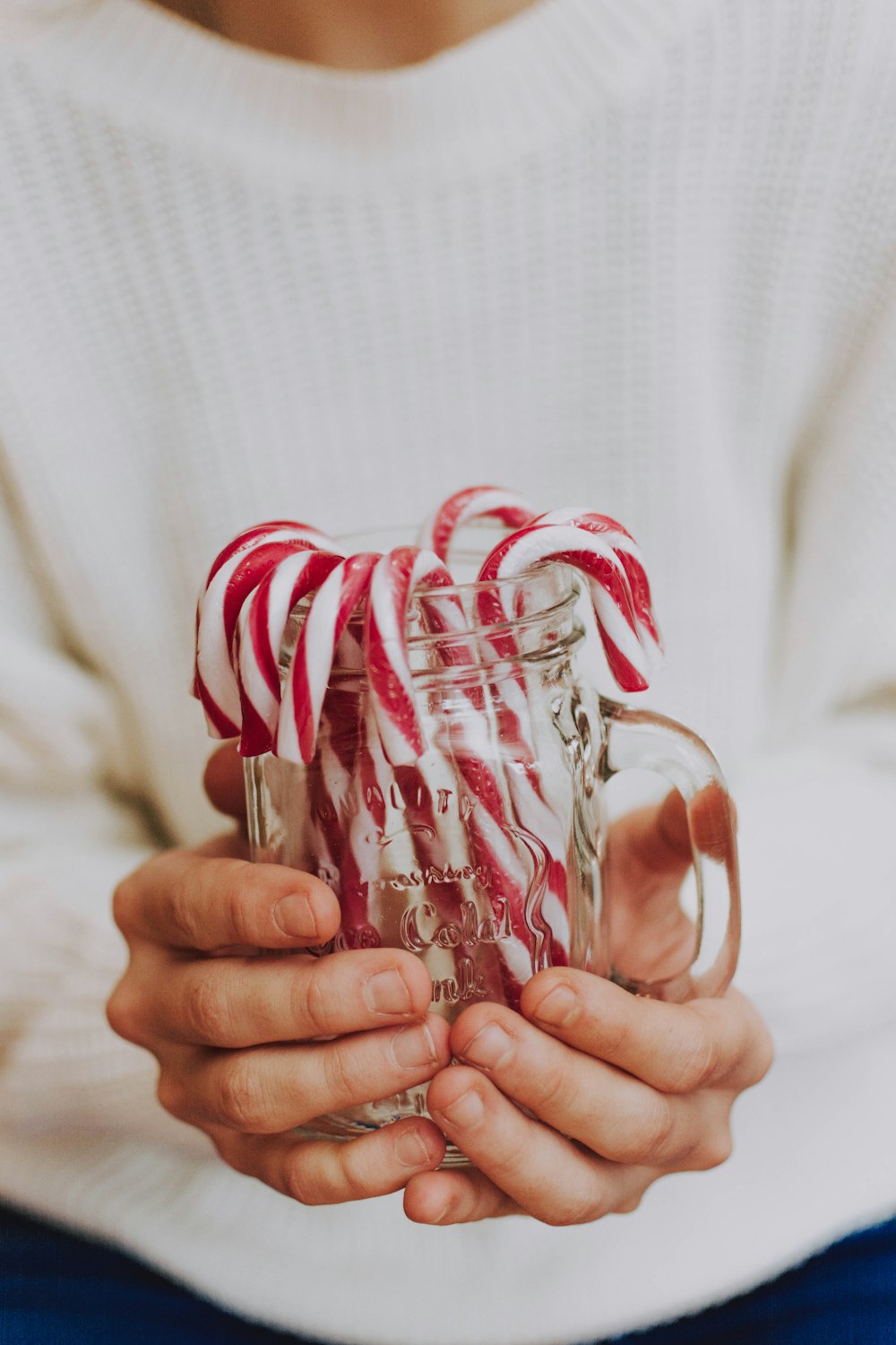 person holding clear glass jar with candy canes