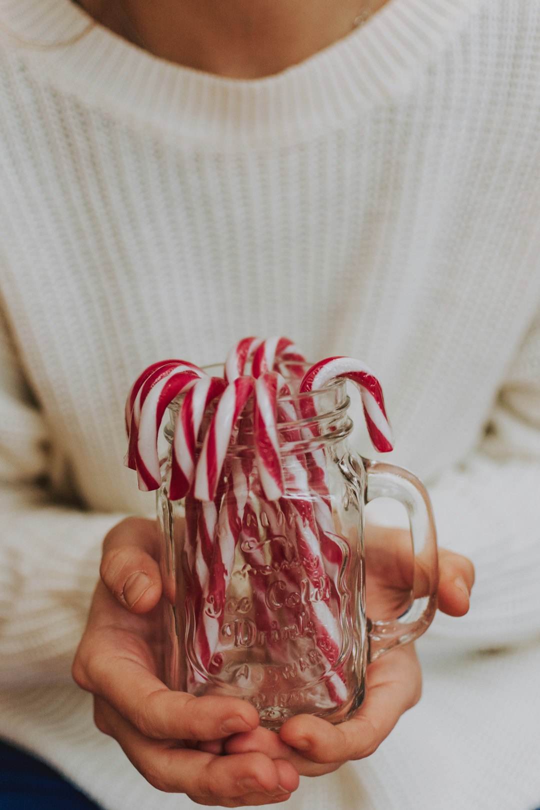 person holding clear glass jar with candy canes