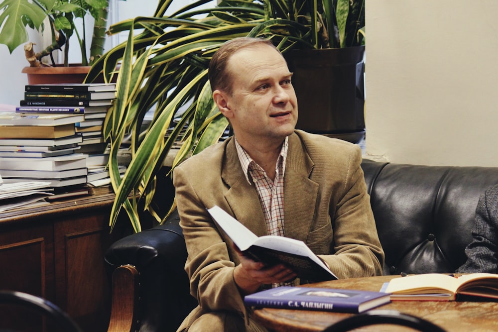 homem segurando o livro enquanto está sentado no sofá de couro preto