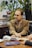 man wearing brown notched lapel suit jacket sitting near brown wooden table