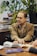 man wearing brown notched lapel suit jacket sitting near brown wooden table