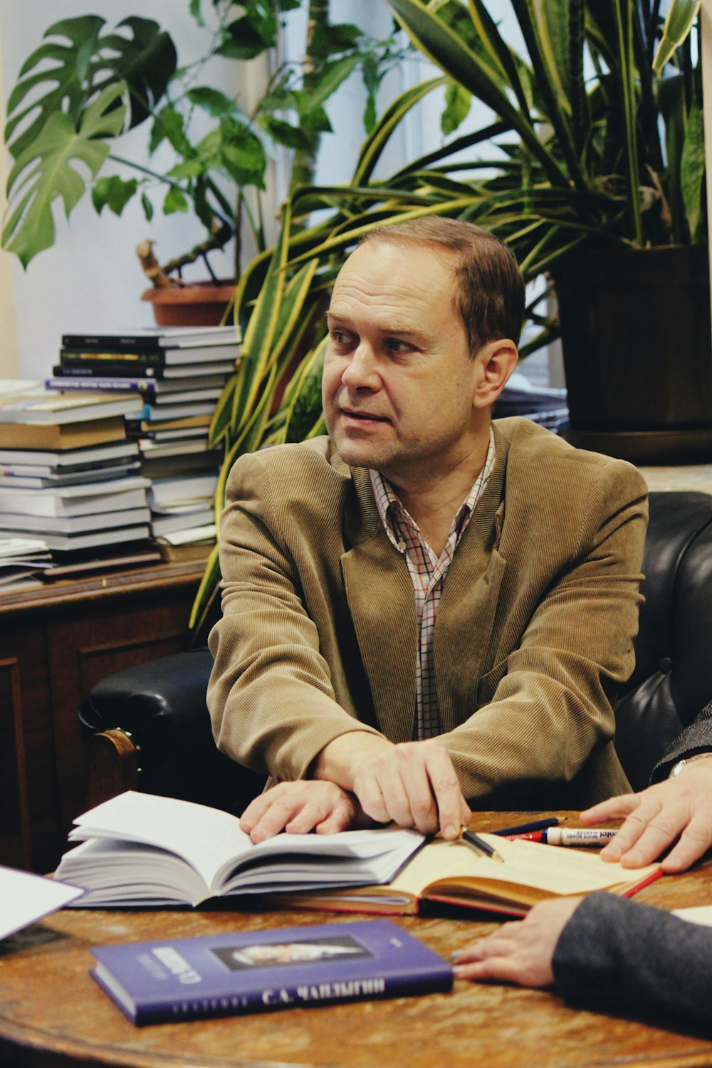 man wearing brown notched lapel suit jacket sitting near brown wooden table