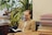 A person reading a book in a cozy, well-lit room filled with plants.