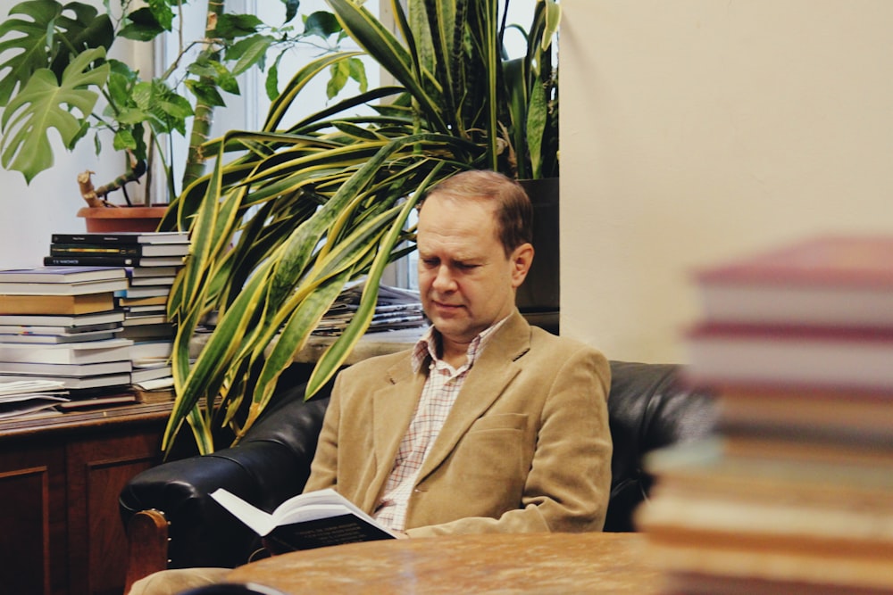 茶色のスエードのノッチ付きラペルスーツジャケットを着て本を読みながら座っている男性