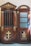 A wooden confessional booth with intricate carvings and religious symbols, including a large cross and the keys of Saint Peter. The word 'PAX' is inscribed at the top. The booth features decorative elements painted in gold, contrasting against the rich brown wood. One side of the booth has a closed door with textured glass panes.