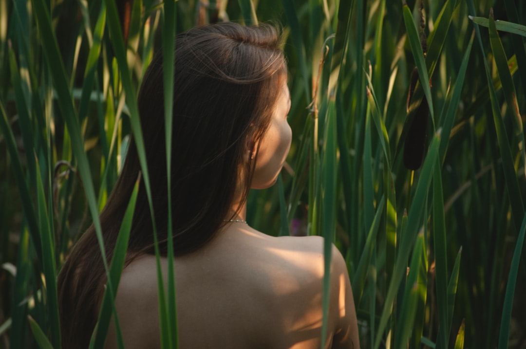 topless woman standing surrounded with green plants while facing back