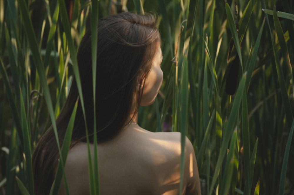 topless woman standing surrounded with green plants while facing back