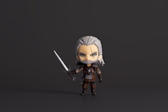 A stylized chibi figure with grey hair and a beard is holding a sword in a defensive stance. The character is dressed in fantasy armor with intricate details and has an intense expression.