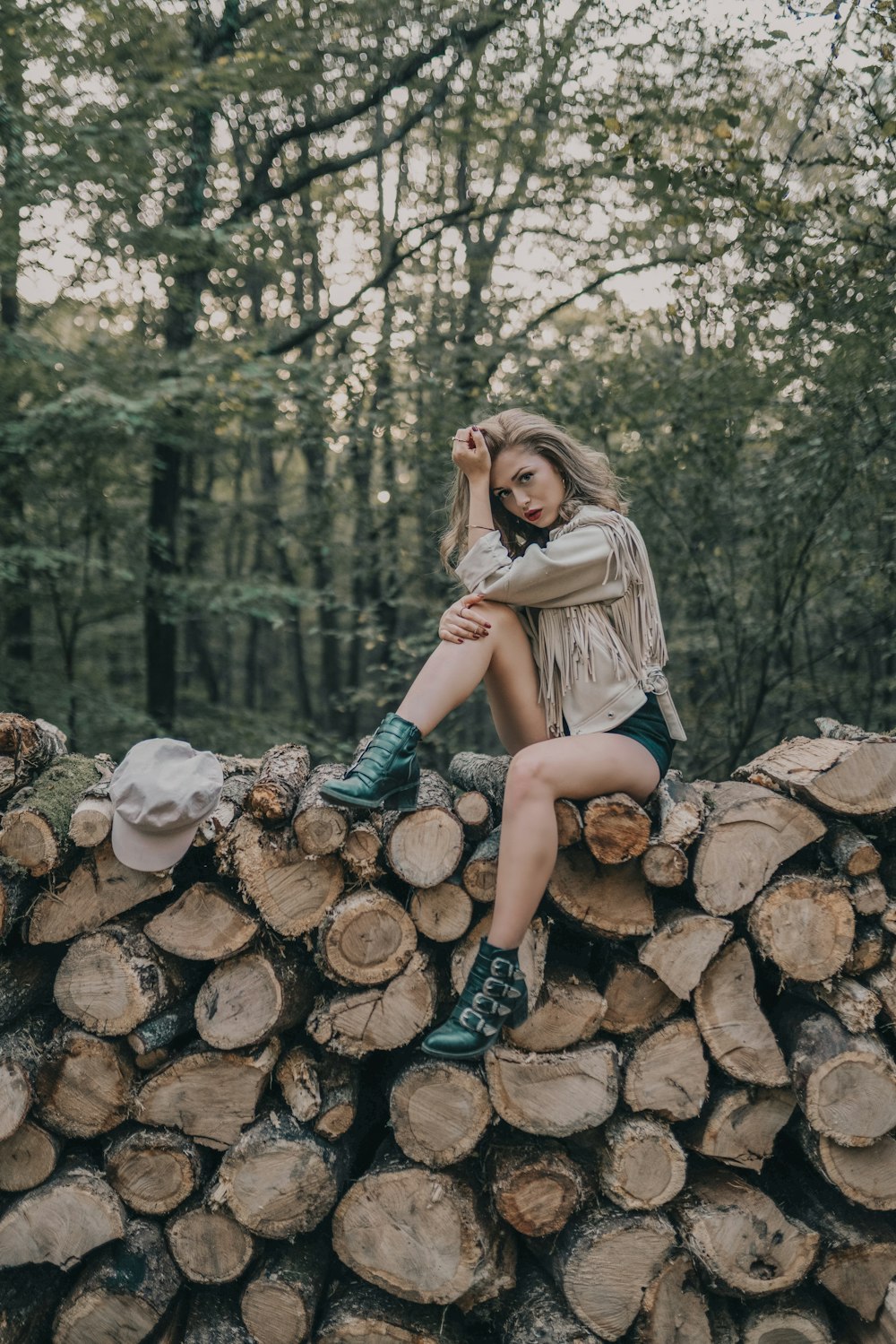 woman sitting on firewood stack surrounded with green trees
