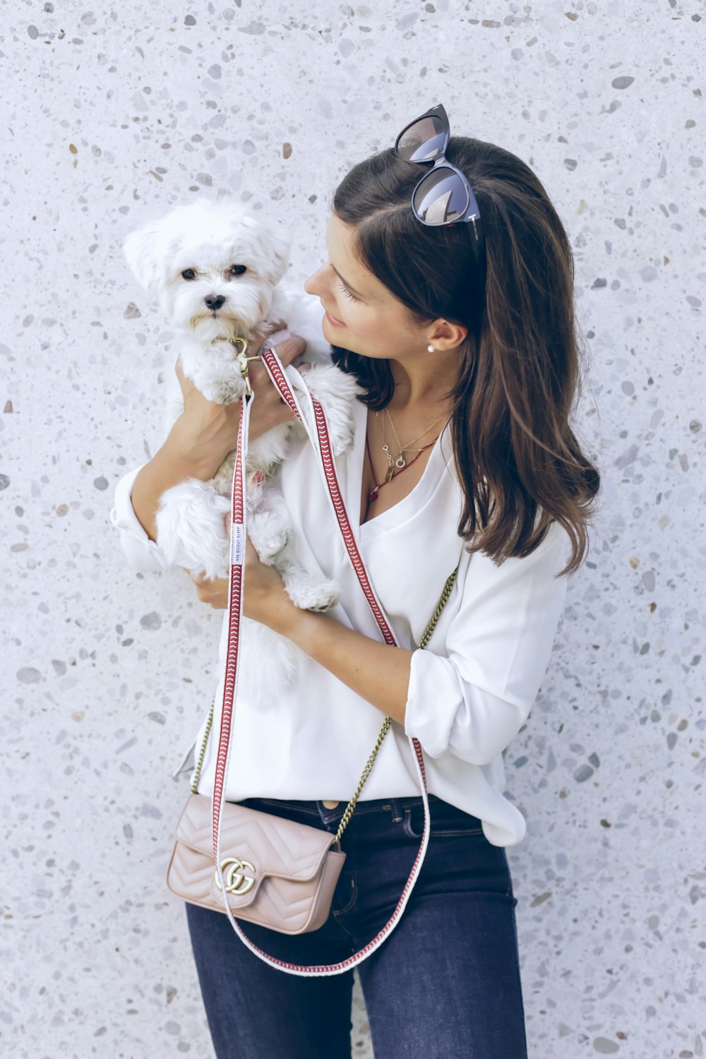 woman in white long-sleeved blouse carrying white puppy beside wall