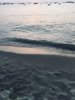 A serene beach at sunset with calm waves and a few scattered boats.