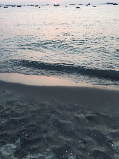 A serene beach at sunset with calm waves and a few scattered boats.