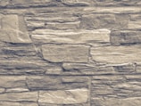 An arrangement of rectangular stones laid out in layers, forming a textured wall pattern. The stones vary in size and exhibit a rugged, rough appearance with natural lines and grooves.