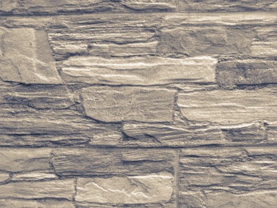 An arrangement of rectangular stones laid out in layers, forming a textured wall pattern. The stones vary in size and exhibit a rugged, rough appearance with natural lines and grooves.