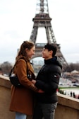 A romantic couple standing in front of the Eiffel Tower in winter.