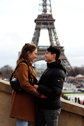 A romantic couple standing in front of the Eiffel Tower in winter.