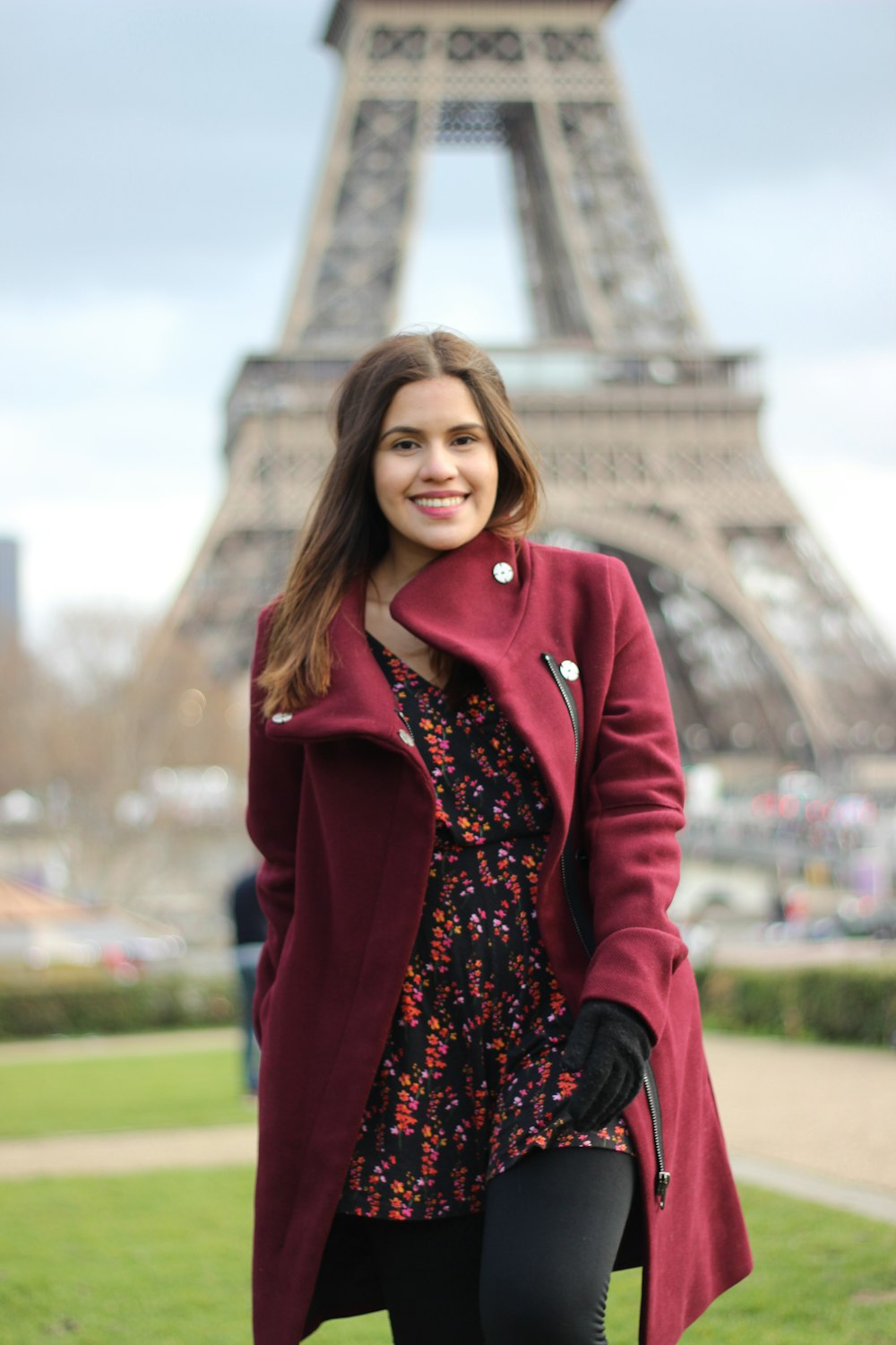 smiling woman wearing maroon coat standing near Eiffel Tower in Paris France