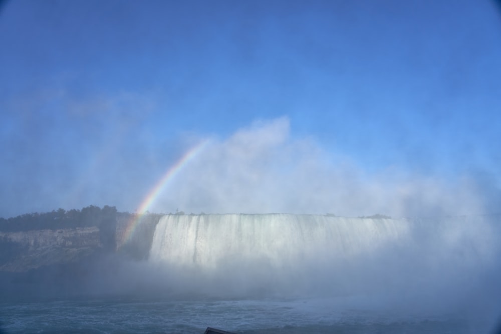 waterfalls with rainbow under blue and white sky
