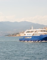 white and blue boat on body of water viewing mountain under white and blue sky