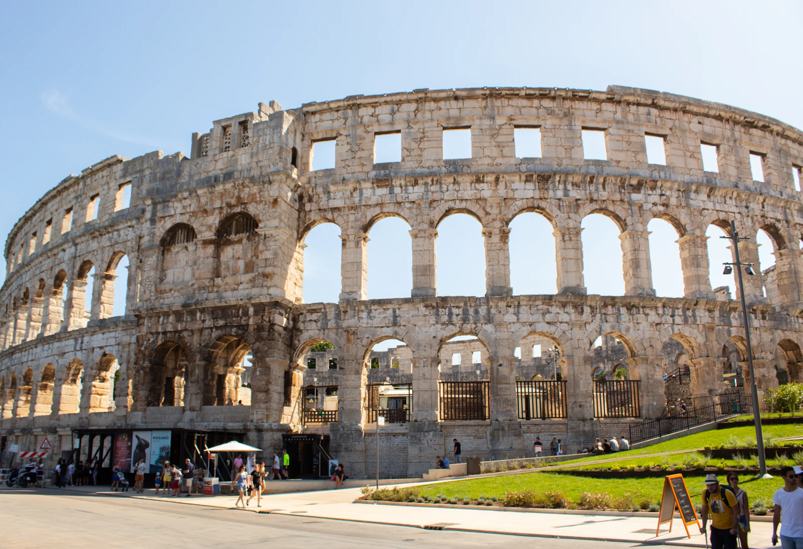 Photograph of The complete outer wall and arches of Pula Arena under a clear blue sky.