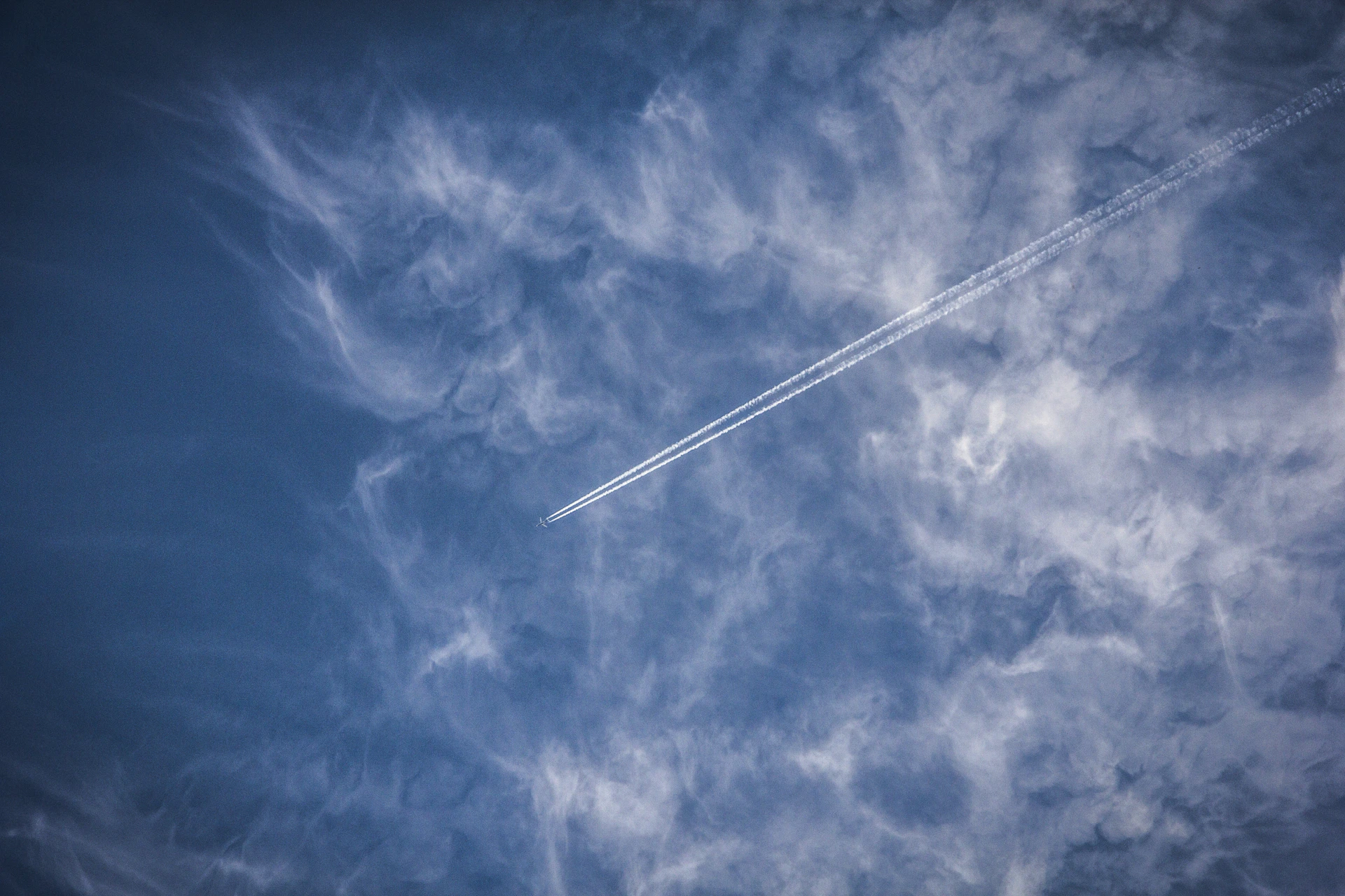 A crisp, clear blue sky dotted with fluffy white clouds and a commercial jet carving a sharp contrail across the horizon.