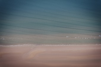 A serene beach scene with gentle waves lapping onto the shore, blending into a gradient of blues and greens in the ocean. Soft sand lines the foreground, creating a tranquil and peaceful atmosphere.
