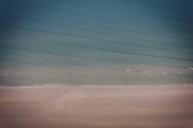 A serene beach scene with gentle waves lapping onto the shore, blending into a gradient of blues and greens in the ocean. Soft sand lines the foreground, creating a tranquil and peaceful atmosphere.